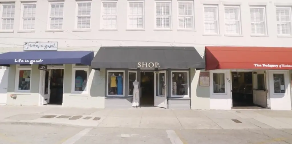 A row of storefronts with a variety of businesses, including a clothing shop, a cafe, and a specialty store, with pedestrians walking on the sidewalk