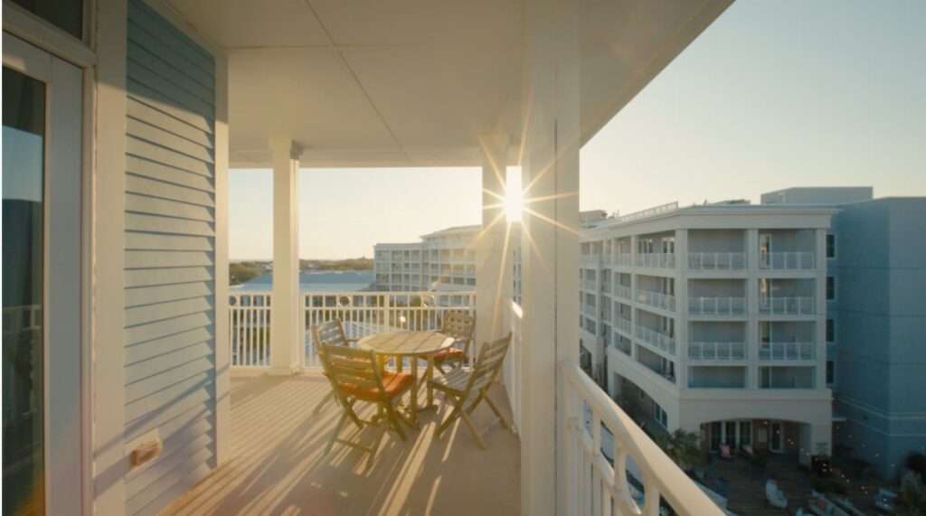 A balcony with a wooden table and chairs overlooking a skyline of high-rise buildings, with the sun shining brightly